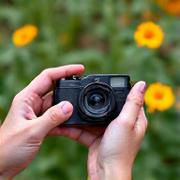 Close-up of hands holding a vintage film camera admiring wildflowers